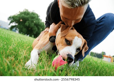 Close-up of a young man hugging a dog. The dog is looking into the frame and holding a ball with its mouth. The love of a man and a dog. American bulldog. - Powered by Shutterstock