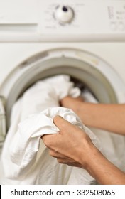 Closeup Of A Young Man Introducing Or Taking Out A White Sheet Into A Washing Machine Or A Clothes Dryer