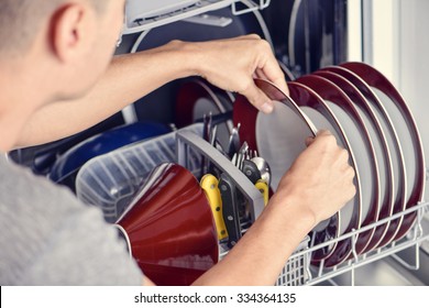 Closeup Of A Young Man Introducing Or Taking Out A Plate Into A Dishwashing Machine