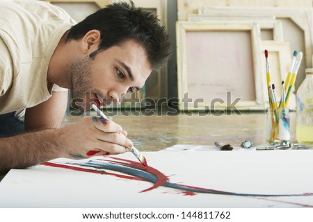 Closeup of a young man painting on canvas on studio floor
