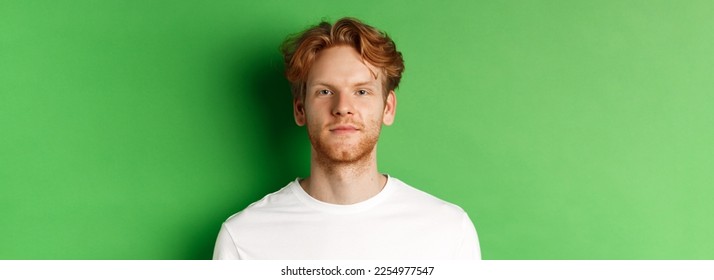 Close-up of young man with red messy hair and beard looking at camera, standing over green background. - Powered by Shutterstock