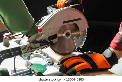 Closeup of young man sawing lumber with sliding compound miter saw indoors.