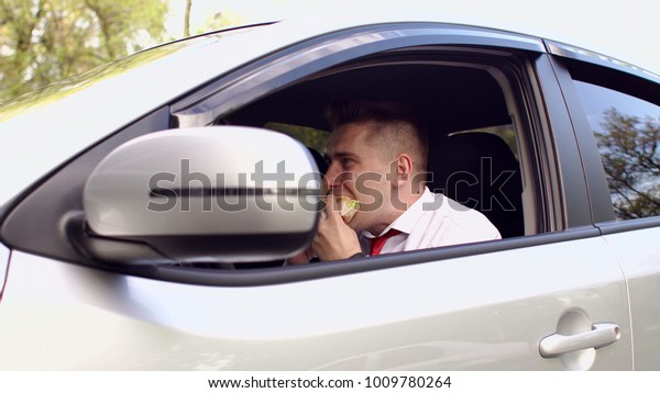 Close-up of young man in shirt\
and tie eating a Burger sitting in the car. Lunch snack in the\
car.