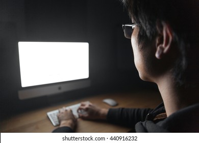 Closeup Of Young Man Sitting And Using Blank Screen Computer In Dark Room