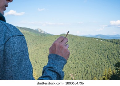 Close-up Of Young Man Smoking Marijuana Joint Outdoors. Hemp Blunt In The Male Hand. Cannabis Is A Concept Of Herbal And Alternative Medicine