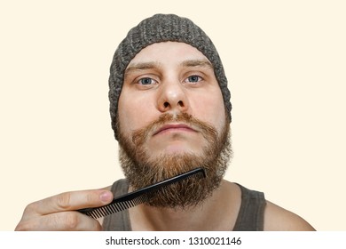Closeup of a young man styling his beard with a comb while standing alone in a studio against a yellow background