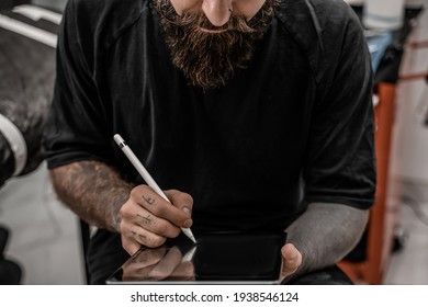 Close-up Young Man Tattoo Artist With Beard Drawing Pencil And Sketch Standing In Workshop Place.