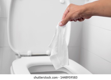 Nahaufnahme eines jungen Mannes, der einen nassen Wischteppich auf die Toilette wirft, in einer weiß gekachelten Toilette