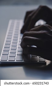 closeup of a young man typing in a computer keyboard in gloom, with a dramatic effect