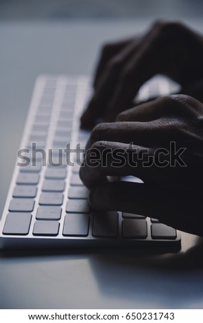 closeup of a young man typing in a computer keyboard in gloom, with a dramatic effect