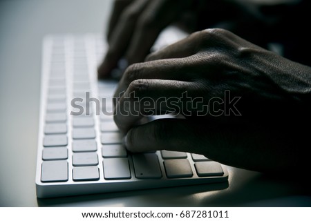 closeup of a young man typing in a computer keyboard in gloom, with a dramatic effect
