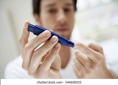 Closeup of young man using lancelet on finger in bathroom