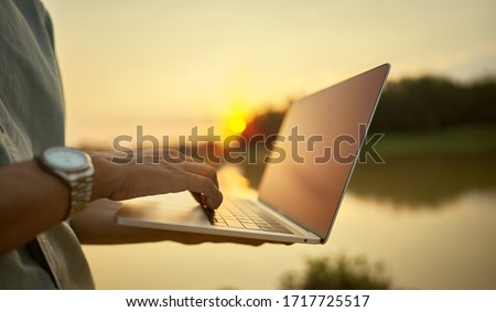   Close-up of a young man using a laptop and the lake and nature at sunset             