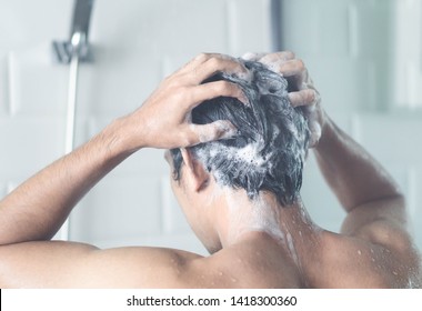 Closeup young man washing hair with with shampoo in the bathroom, vintage tone, selective focus
