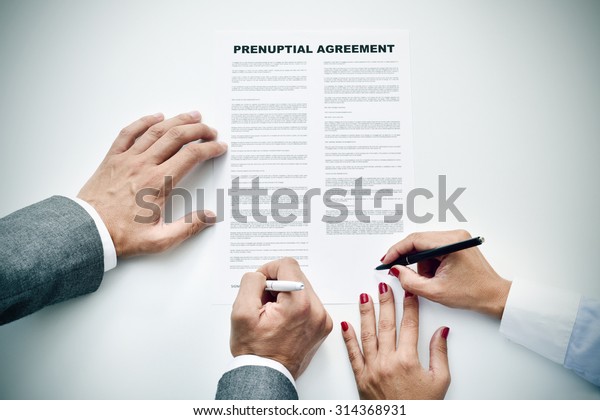 closeup of a young man an a young woman signing\
a prenuptial agreement