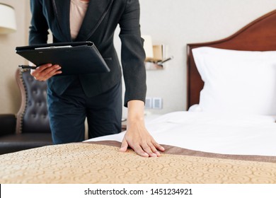 Close-up Of Young Manager In Black Suit Holding Folder With Documents And Checking The Quality Of Blanket On The Bed In The Hotel Room