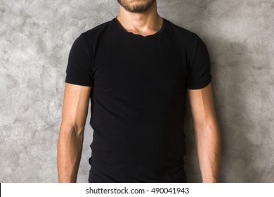 Closeup of young man's body in empty black t-shirt on textured concrete wall background. Mock up