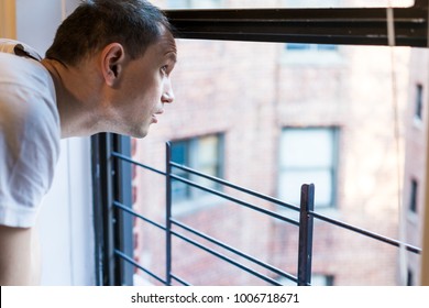 Closeup Of Young Man's Face Looking Outside Of Small Apartment Window In New York City NYC Urban Bronx, Brooklyn Brick Housing, Guard Rail, Security Bars, Checking Weather