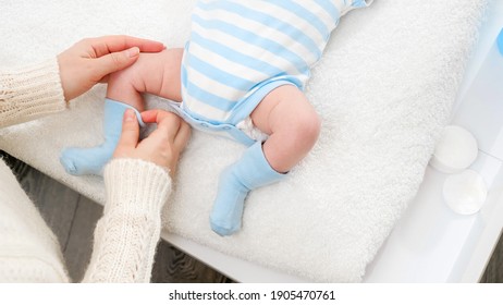 Closeup of young mother dressing her little baby son in socks while changing clothes on table. Concept of babies and newborn hygiene and healthcare. Caring parents with little children - Powered by Shutterstock