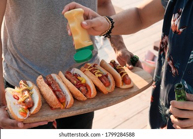 Close-up of young people adding sauce on hot dogs they preparing food for the party outdoors - Powered by Shutterstock