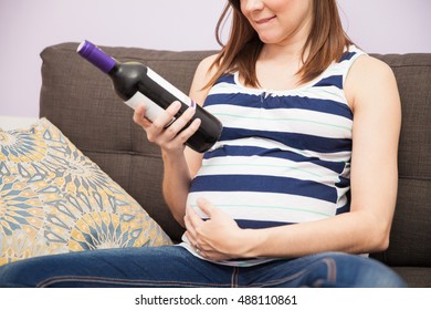 Closeup of a young pregnant woman looking at a bottle of wine and trying to keep herself from drinking