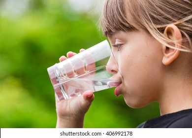 Close-up Of Young Scandinavian Child Drinking Fresh And Pure Tap Water From Glass With A Blurred Green Background.