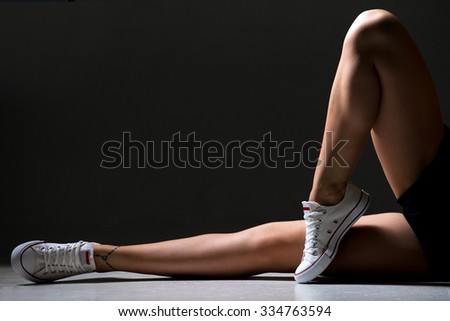 Close-up of young slim sporty beautiful woman legs working out in stylish cool white training shoes, studio image on grey background
