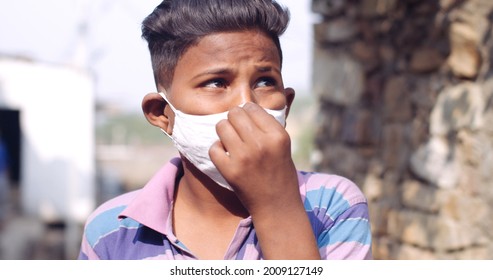 A Closeup Of A Young South Asian Child Fixing His Covid-19 Mask While Looking Away From The Camera