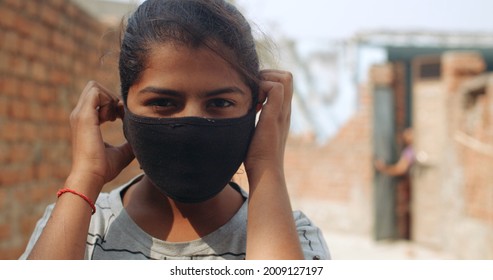 A Closeup Of A Young South Asian Child Tucking Her Covid Mask Behind Her Ears On A Blurry Background