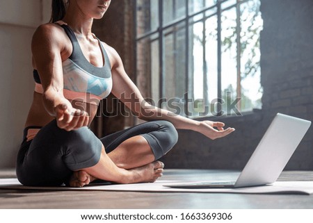 Closeup young sporty fit slim woman coach do practice video online training hatha yoga instructor modern laptop meditate Sukhasana posture relax breathe easy seat pose gym healthy lifestyle concept.