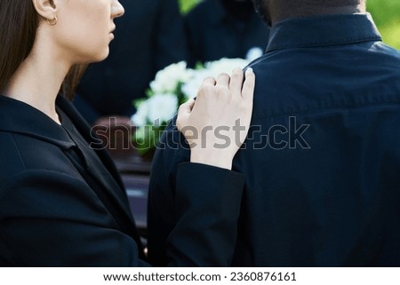 Close-up of young supporting woman consoling her grieving friend wearing mourning clothes at funeral of his wife or other family member