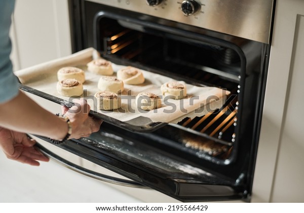 Close-up\
of young woman baking sweet buns in oven at\
home