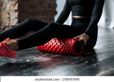 Close-up of a young woman in a black tracksuit performs a warm-up exercise by putting a roller massager for the fascia of the muscles of the body under the hips