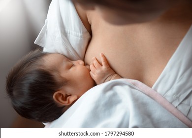 Close-up young woman breastfeeding her baby on blurred background.