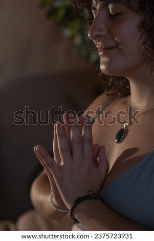 Close-up of a young woman with brown curly hair with her hands in prayer in a meditative pose at chest height