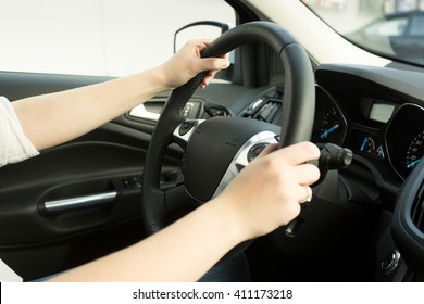 Closeup of young woman driving car and holding hands on steering wheel