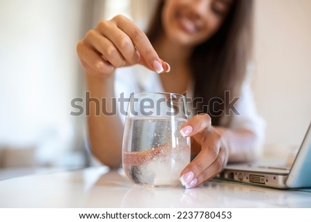 Closeup of a young woman dropping an effervescent antacid in a glass of water. young woman hardly put a soluble pill with a medicine for pain or a hangover in a glass of water