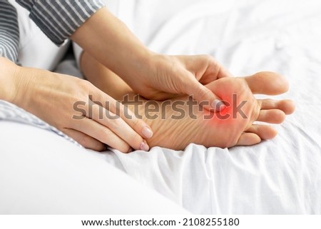 Close-up of a young woman feeling pain when pressing on her foot. Painful female legs from uncomfortable tight shoes and high heels, sprains, spasms. Healthcare, health problems, inflammation concept.