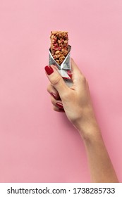 Close-up of young woman hand holding cereal bar on pastel pink background. Sweet healthy food.