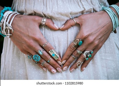 closeup of young woman hands in heart shape with lot of boho style jewelry, rings and bracelets outdoor summer day