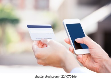 Closeup Young Woman Hands Holding Credit Card And Using Cell, Smart Phone For Online Shopping Or Reporting Lost Card, Fraudulent Transaction, Isolated City Outside Background. New Generation Gadget