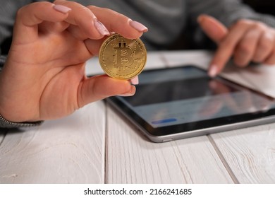 Close-up of a young woman holding a golden bitcoin and working with charts on a tablet. Bitcoin Cryptocurrency investment concept. - Shutterstock ID 2166241685