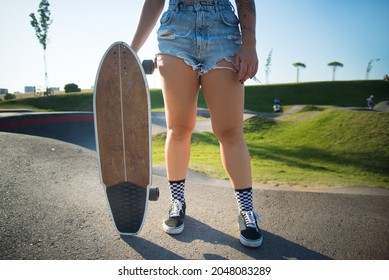 Close-up of young woman holding longboard. Girl in checkered socks and shorts holding skateboard. Sport, hobby, active lifestyle concept