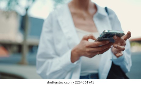 Closeup of young woman holds smartphone in her hands and scrolls through the news feed. Close-up of girl hand uses mobile phone outdoors - Shutterstock ID 2264561945