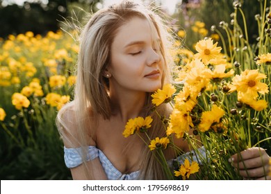 Close-up of a young woman with long blonde hair, sitting in a garden, smelling yellow flowers in sun light. - Powered by Shutterstock