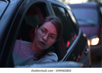 Close-up of a young woman looking through a car window in a night traffic jam. rush hour