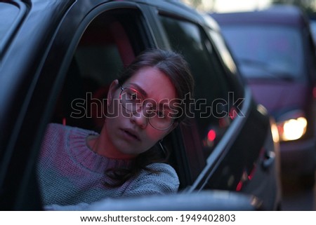 Close-up of a young woman looking through a car window in a night traffic jam. rush hour