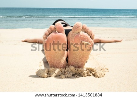 Close-up Of A Young Woman Lying On The Sand With Her Messy Feet On Beach