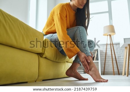 Close-up of young woman massaging her tired feet while sitting on the couch at home