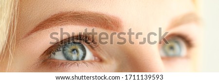 Close-up of young woman with perfect light brown eyebrow looking up. Macro shot of female after beauty facial procedure. Permanent makeup cosmetology and wellness concept